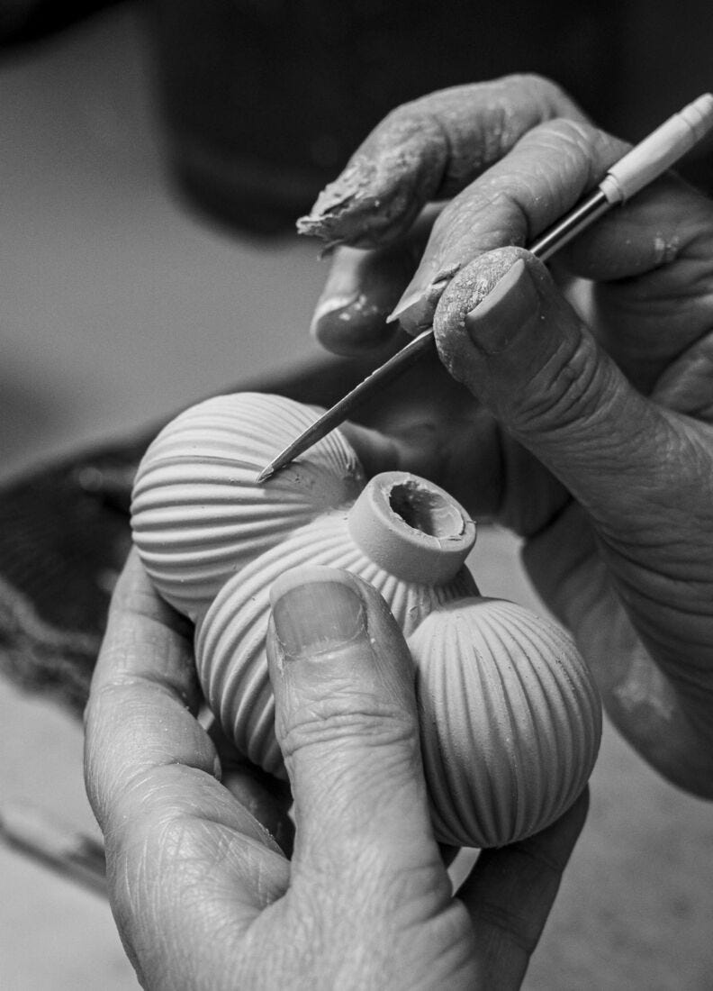 A craftsperson's hands hand-painting a ribbed porcelain lamp shade in the Lladró workshop, in black and white