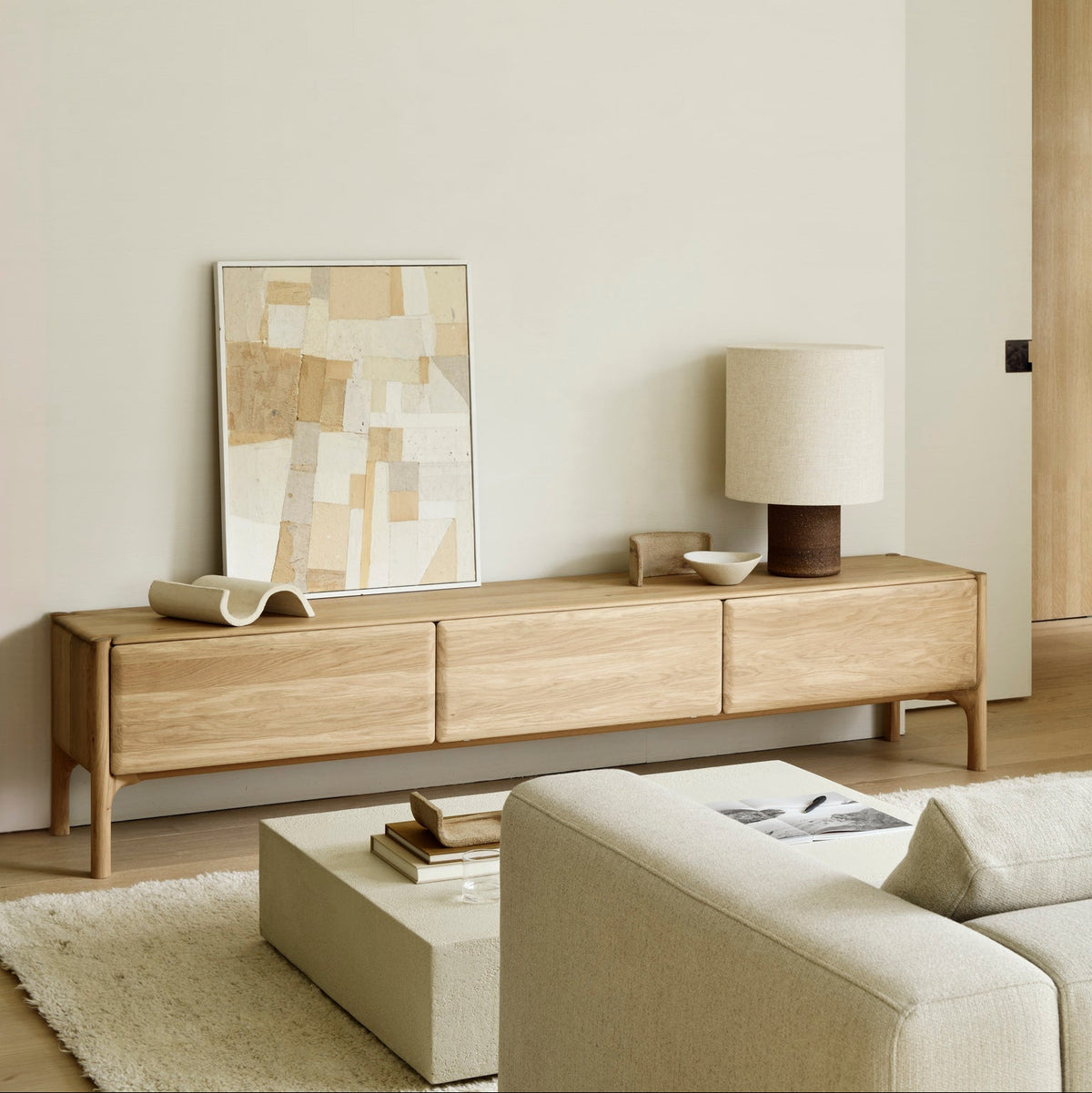 Ethnicraft PI TV cupboard in FSC-certified solid oak, low and wide beneath framed art, with a sofa and coffee table in a bright living room