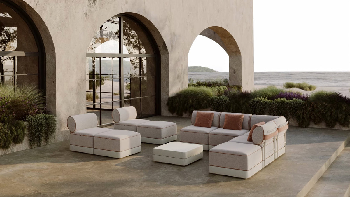 Pale modular outdoor sofas and low tables arranged under a stone arcade looking out to the sea