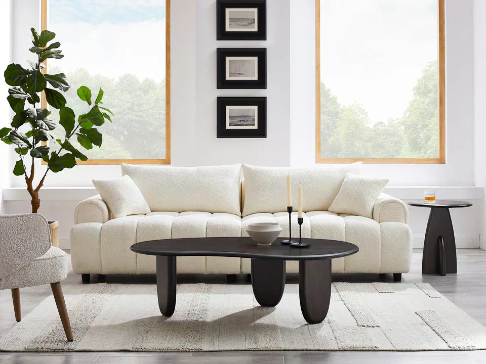 A white sofa with a dark oval coffee table and side tables in a bright, neutral living room