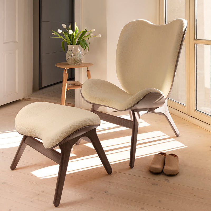 UMAGE A Conversation Piece lounge chair in dark oak with textured upholstery and matching ottoman, styled in a warm-toned living room
