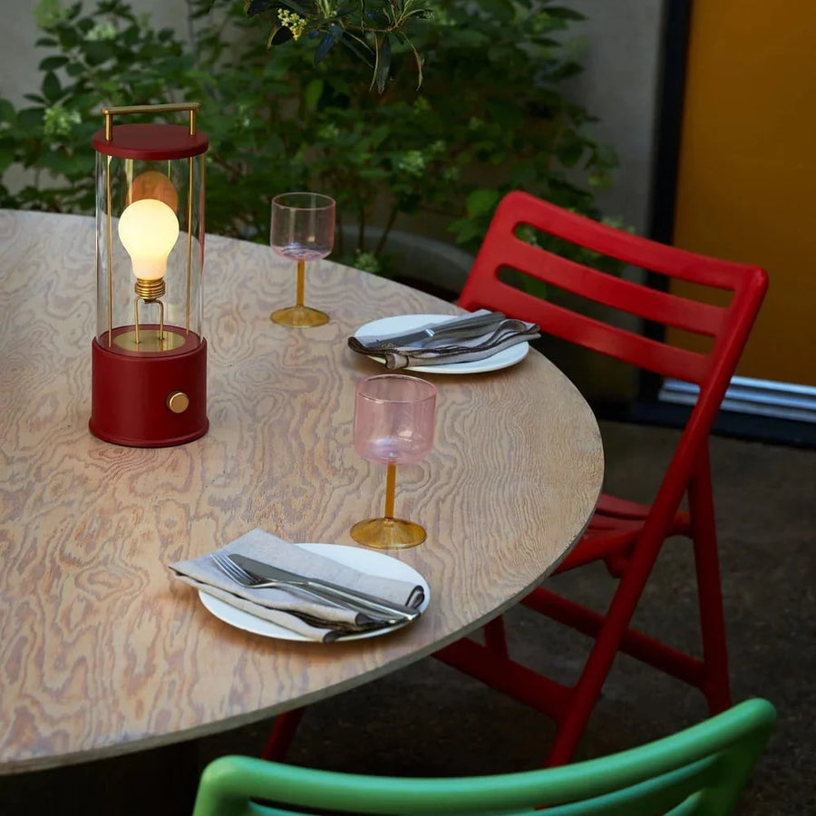 Tala Muse cordless lamp in Pomona Red, lit on a round wooden dining table set with plates and pink glasses
