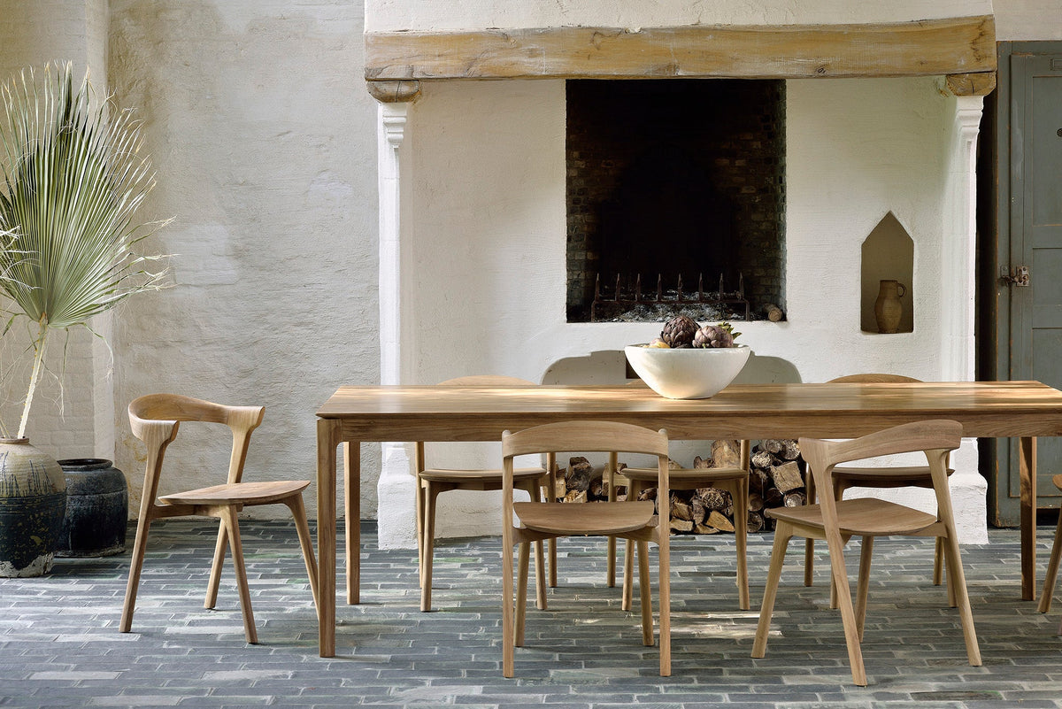 An oak dining table and chairs in front of a stone fireplace in a whitewashed room