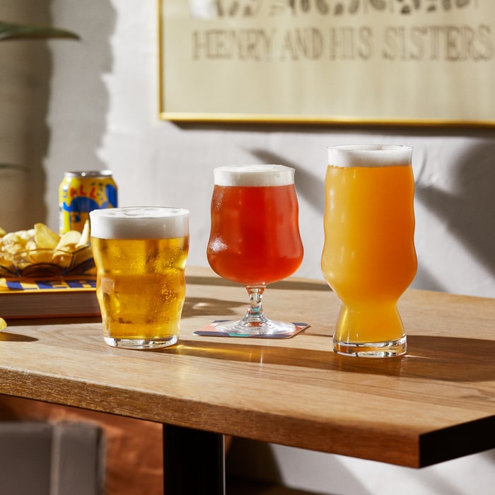 Three glasses of beer on a wooden table beneath a framed lettering artwork