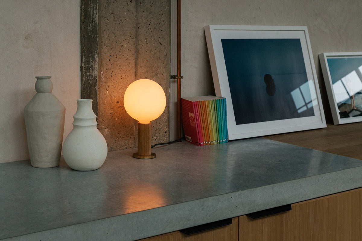 A glowing globe table lamp on a concrete counter beside pale ceramic vases and framed prints