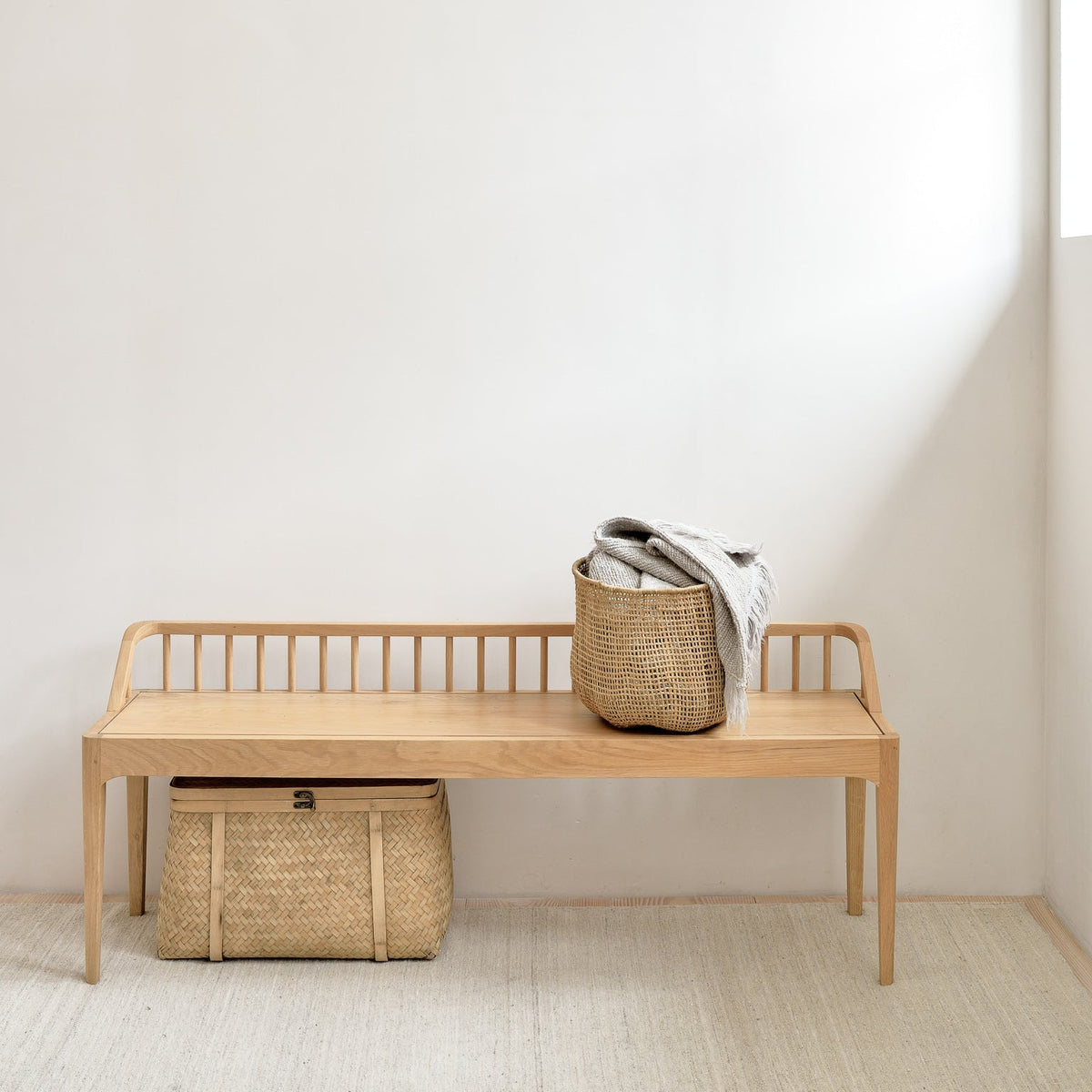 Ethnicraft Spindle bench in oak with woven baskets against a white wall