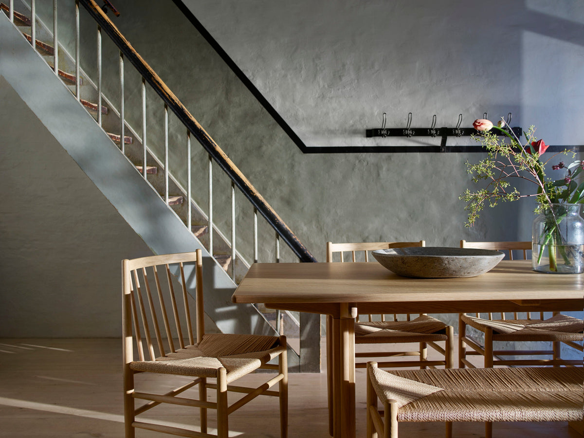 A pale oak dining table with woven paper-cord chairs beside a staircase in a green-walled Scandinavian interior
