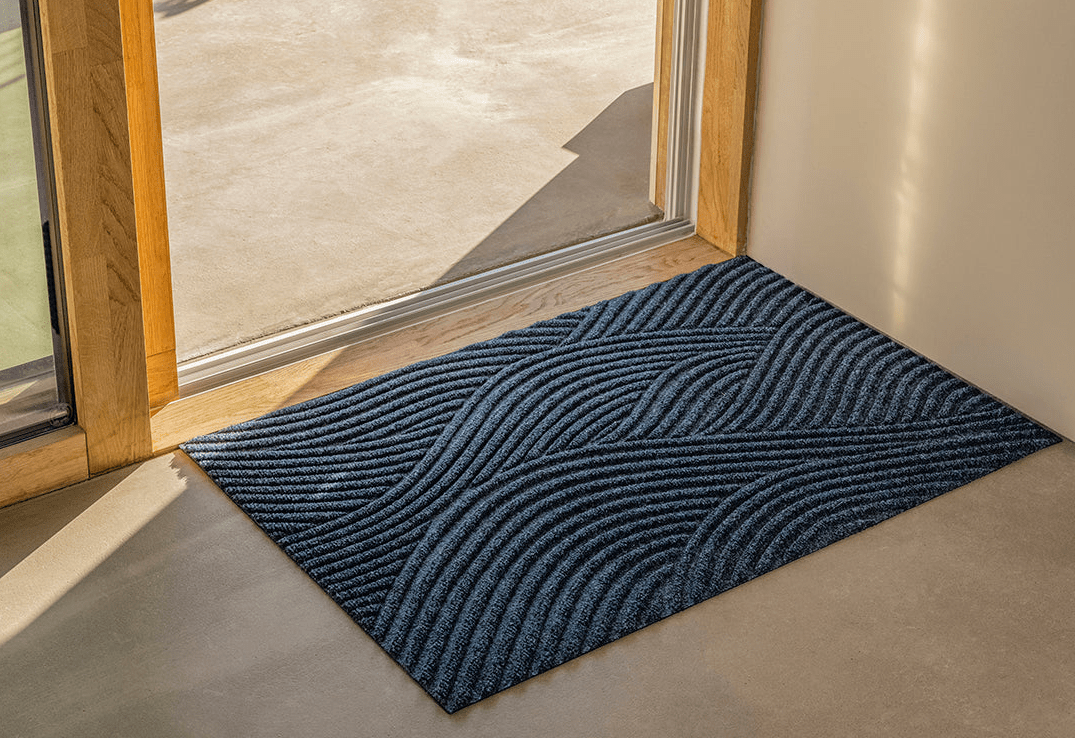 A navy patterned all-weather doormat in a sunlit doorway