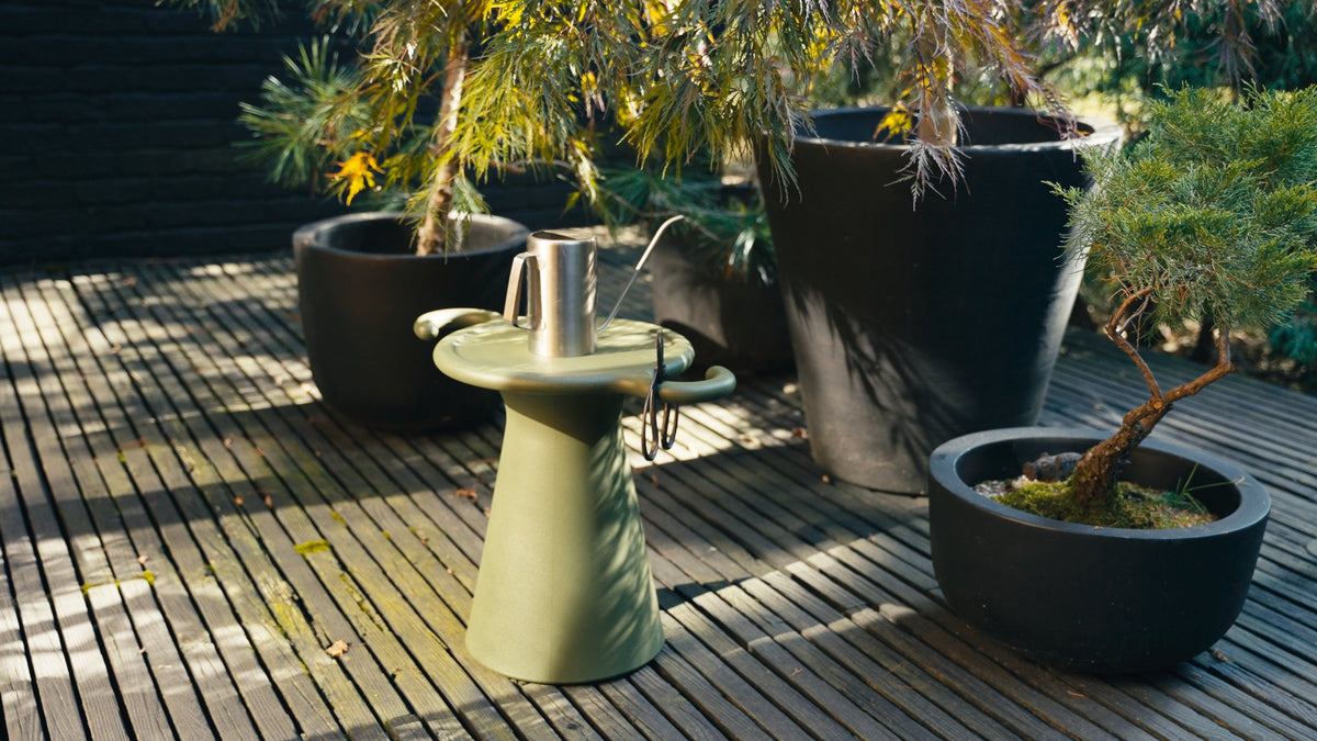 A pale green side table on a wooden deck beside large dark planters