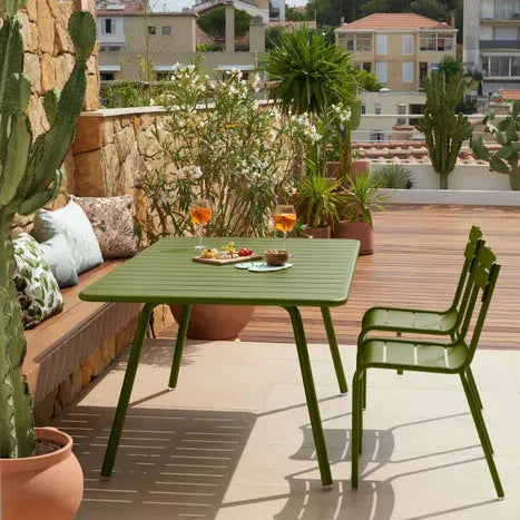 A green powder-coated outdoor dining table and chairs on a Mediterranean terrace surrounded by cacti and potted plants