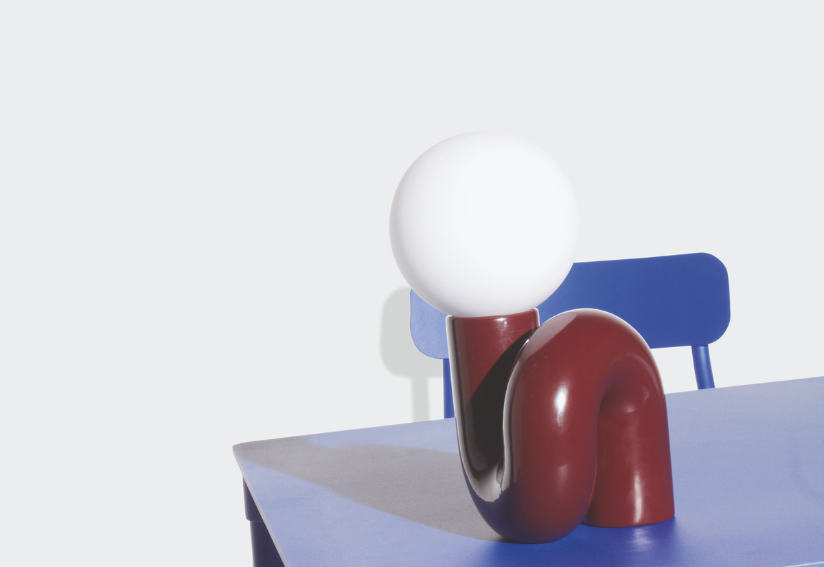 A sculptural red table lamp with a glass globe shade on a blue table