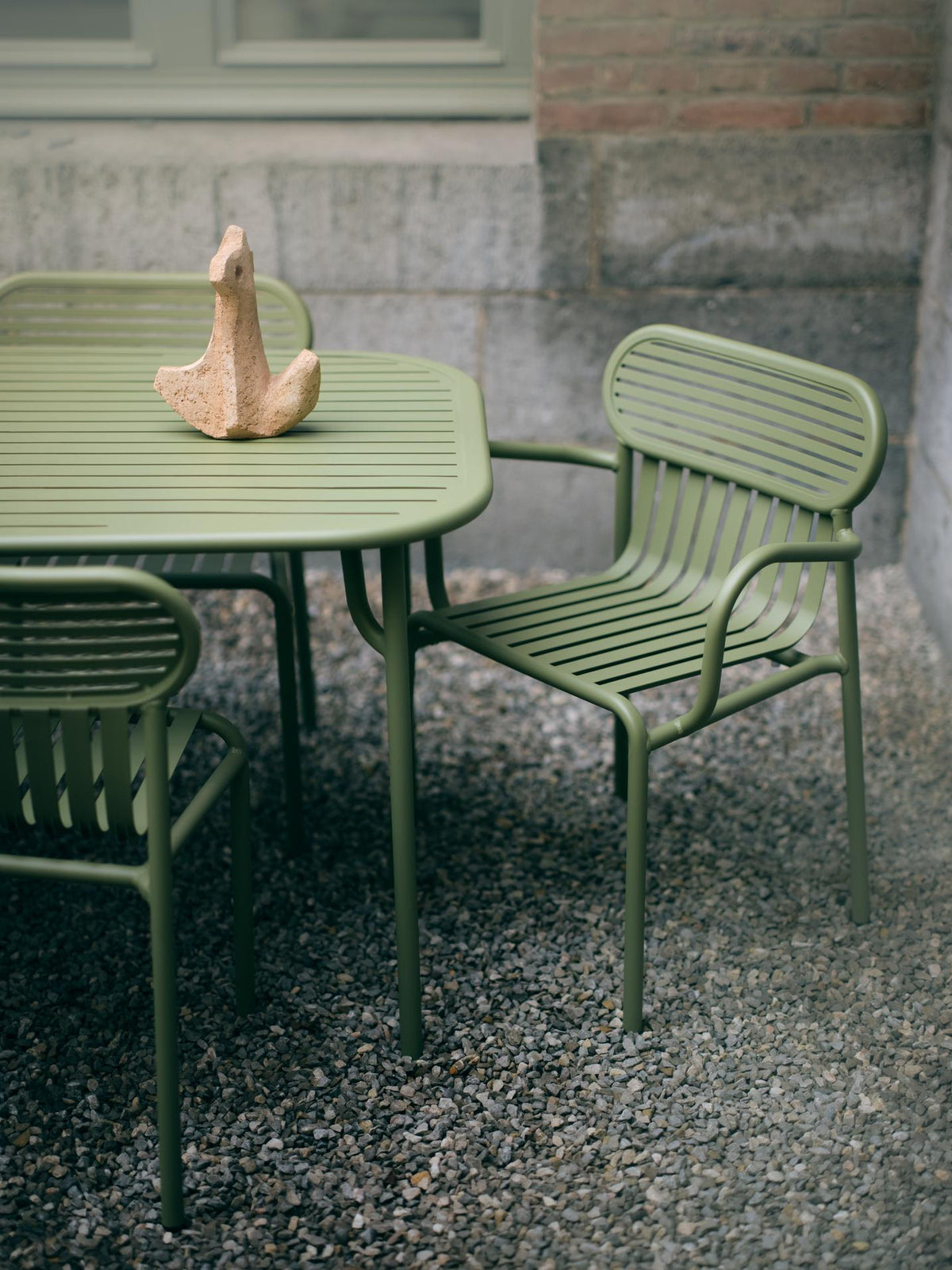 A green metal outdoor table and chair on terrazzo paving
