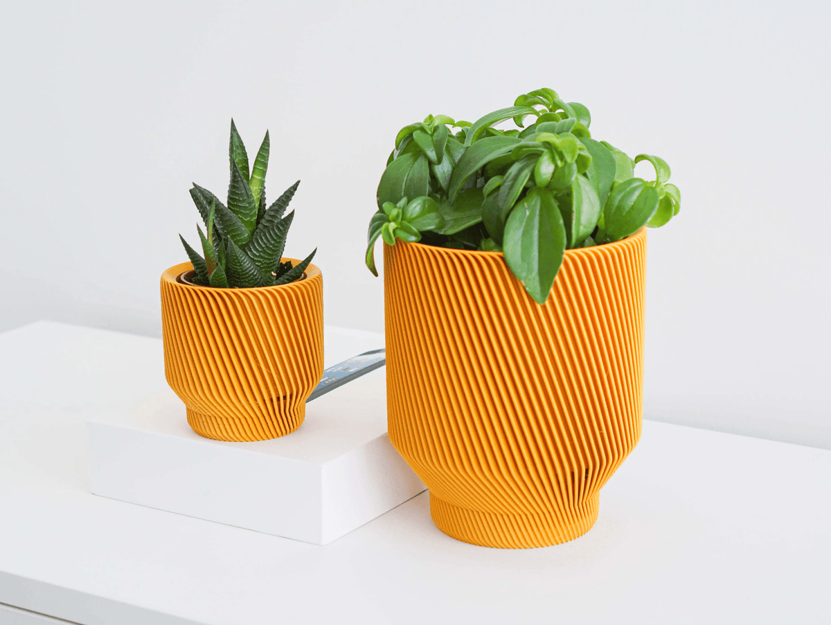 Two orange 3D-printed planters holding a succulent and basil on a white surface