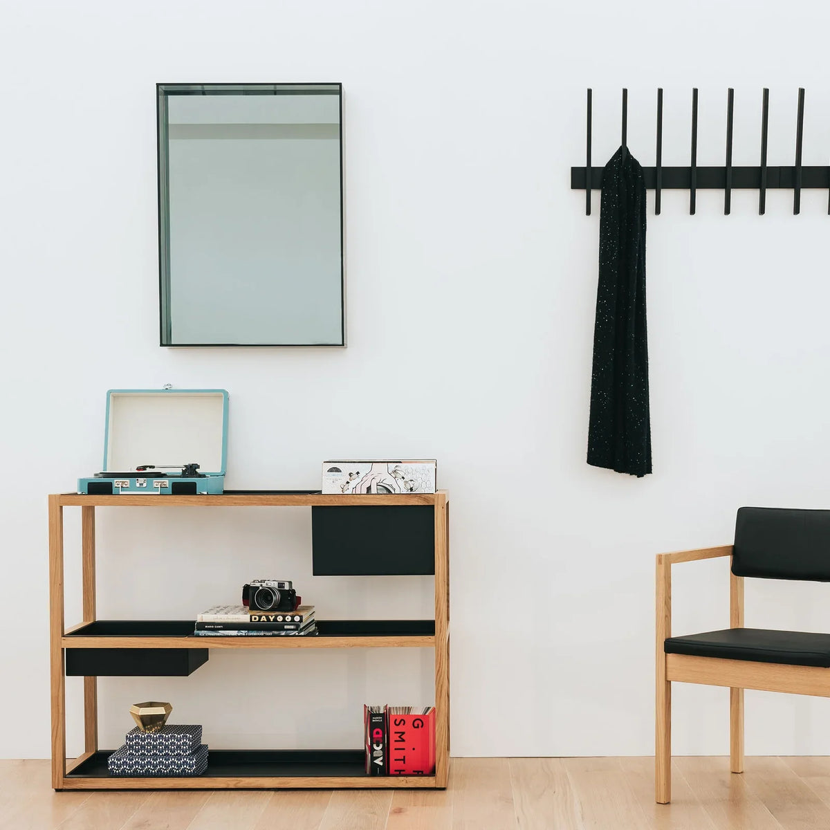 An entryway styled with a Case Fin coat hook, a wall mirror, an open shelving unit and a wooden armchair