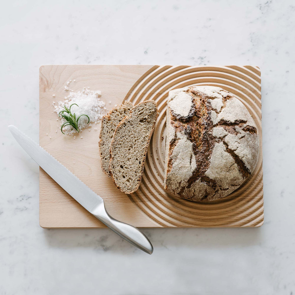Sliced sourdough on a ribbed wooden serving board with a knife on a marble counter