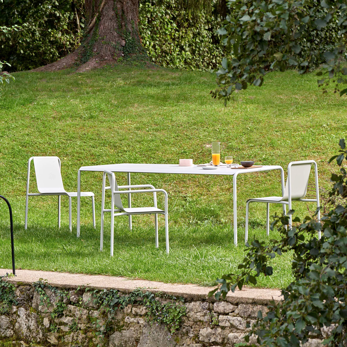 Tiptoe PANORAMA Outdoor Chairs in Chalk Gray around a table in a garden, powder-coated steel