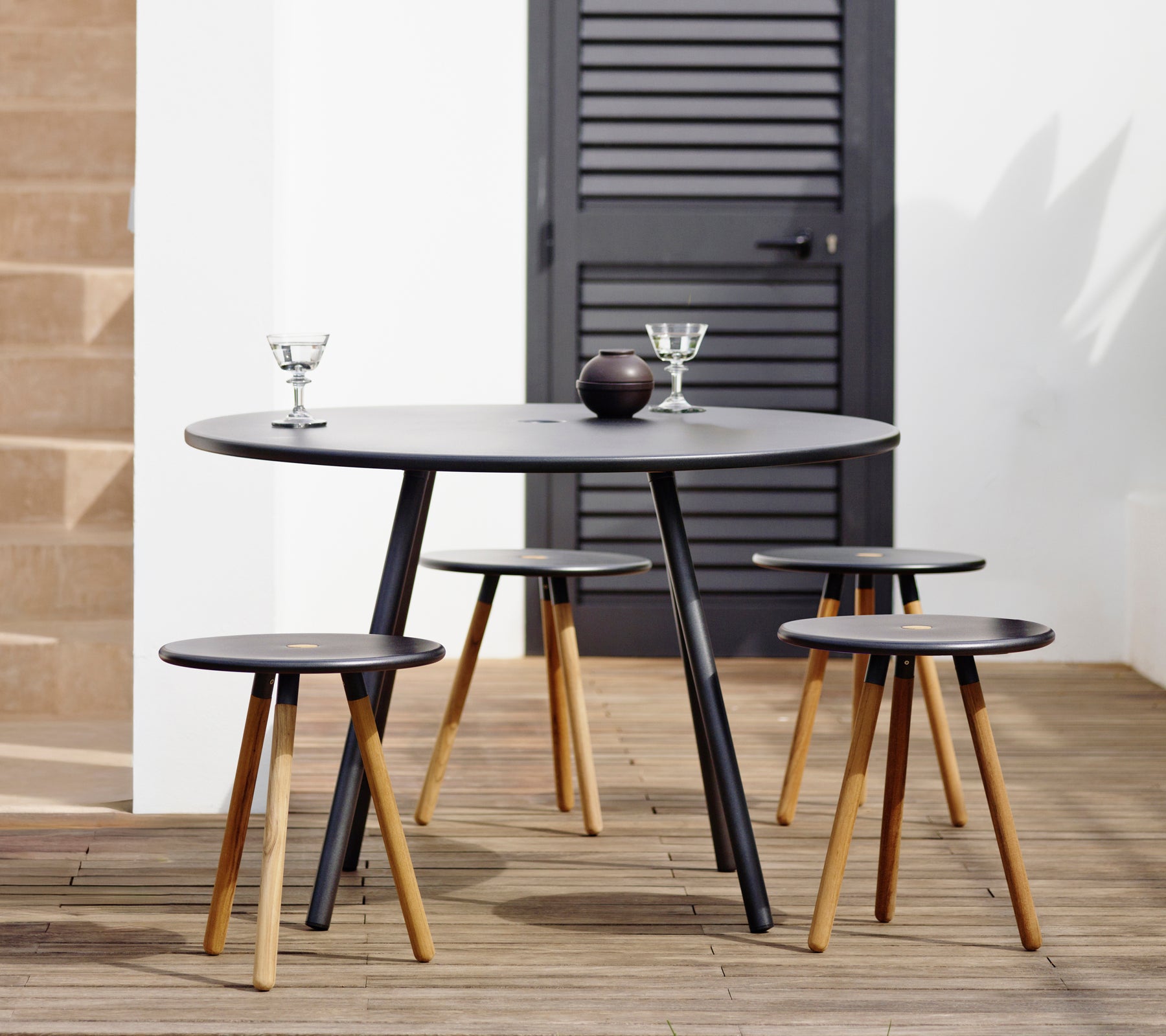 Round black table with four matching stools on a wooden deck.