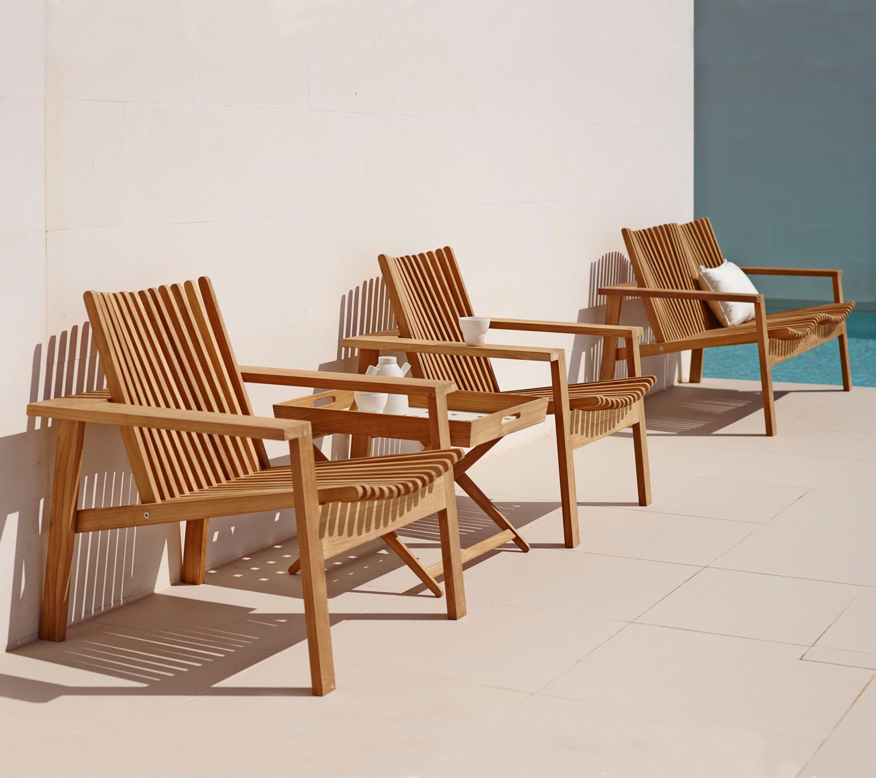 Wooden outdoor chairs on a patio with a pool in the background