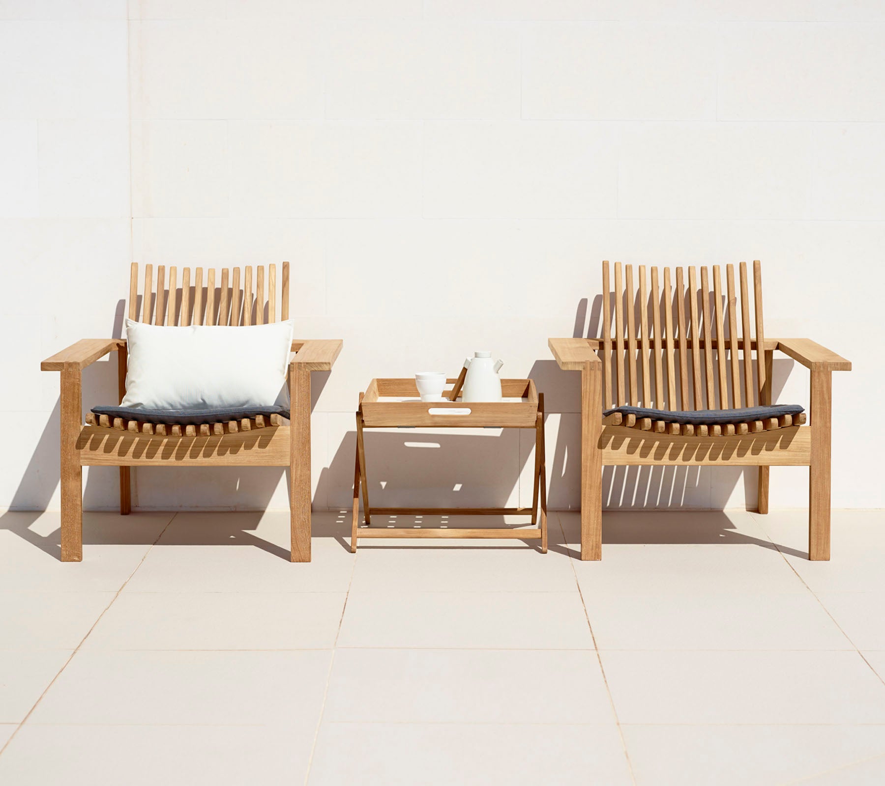 Two wooden chairs with cushions and a small table on a white background