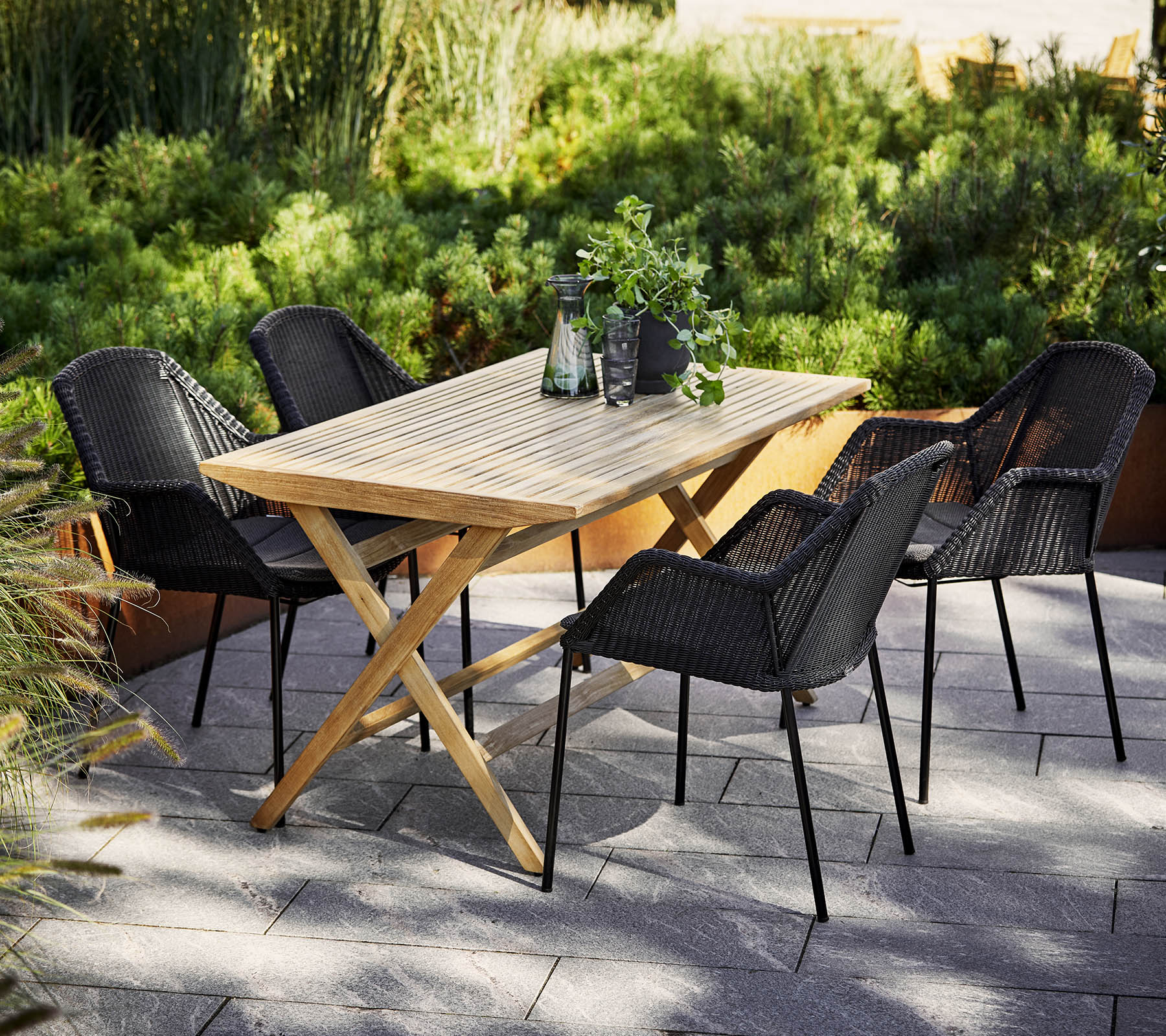 Cane-line wooden slatted dining table set with black chairs, sustainable garden furniture Comosum