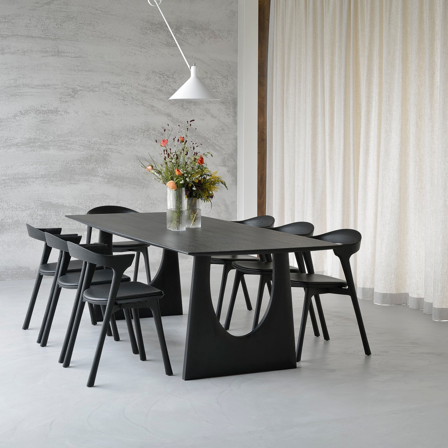 Modern black dining table with chairs in a minimalistic room with concrete wall and white curtain.
