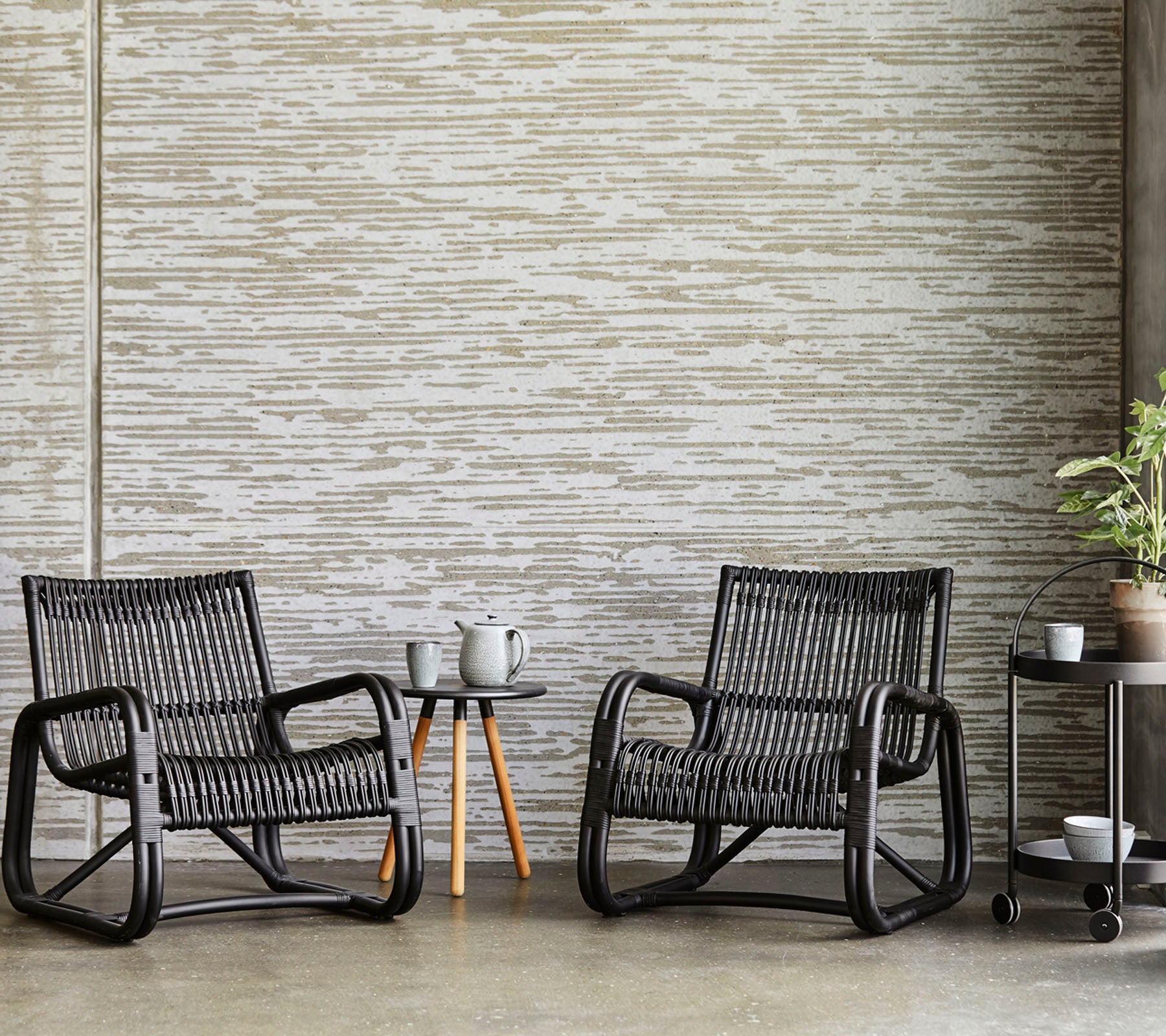 Two wicker chairs with a small table against a textured wall.
