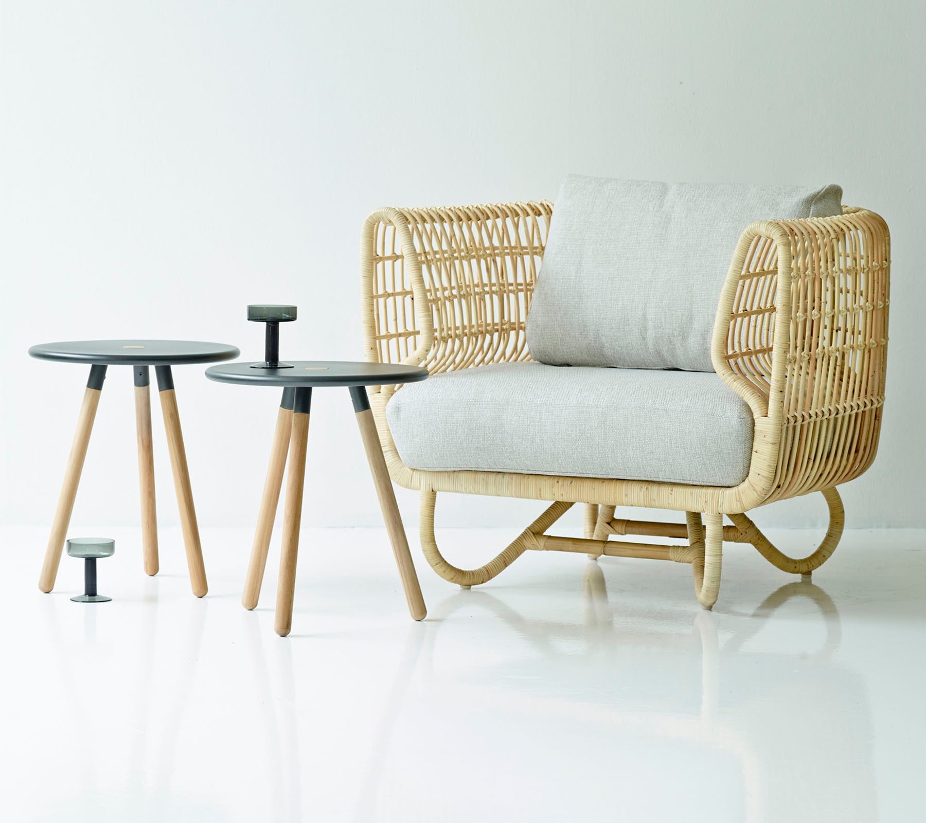 Wicker chair with white cushion and two small round tables on a white background
