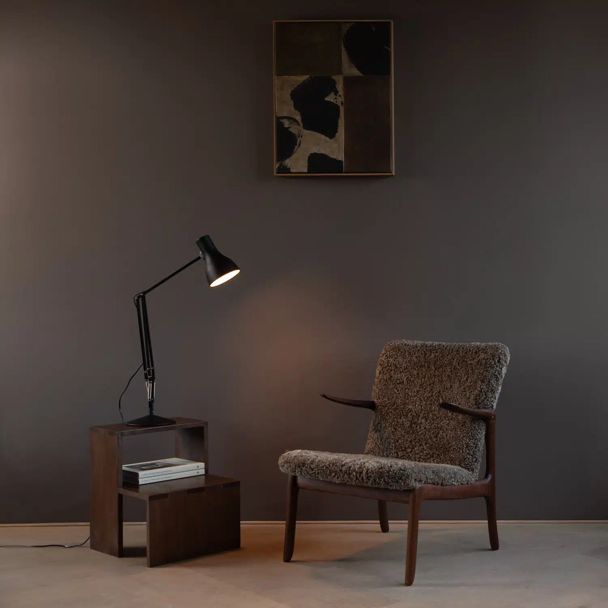 Anglepoise Type 75 desk lamp in black on a dark wood side table beside a shearling armchair