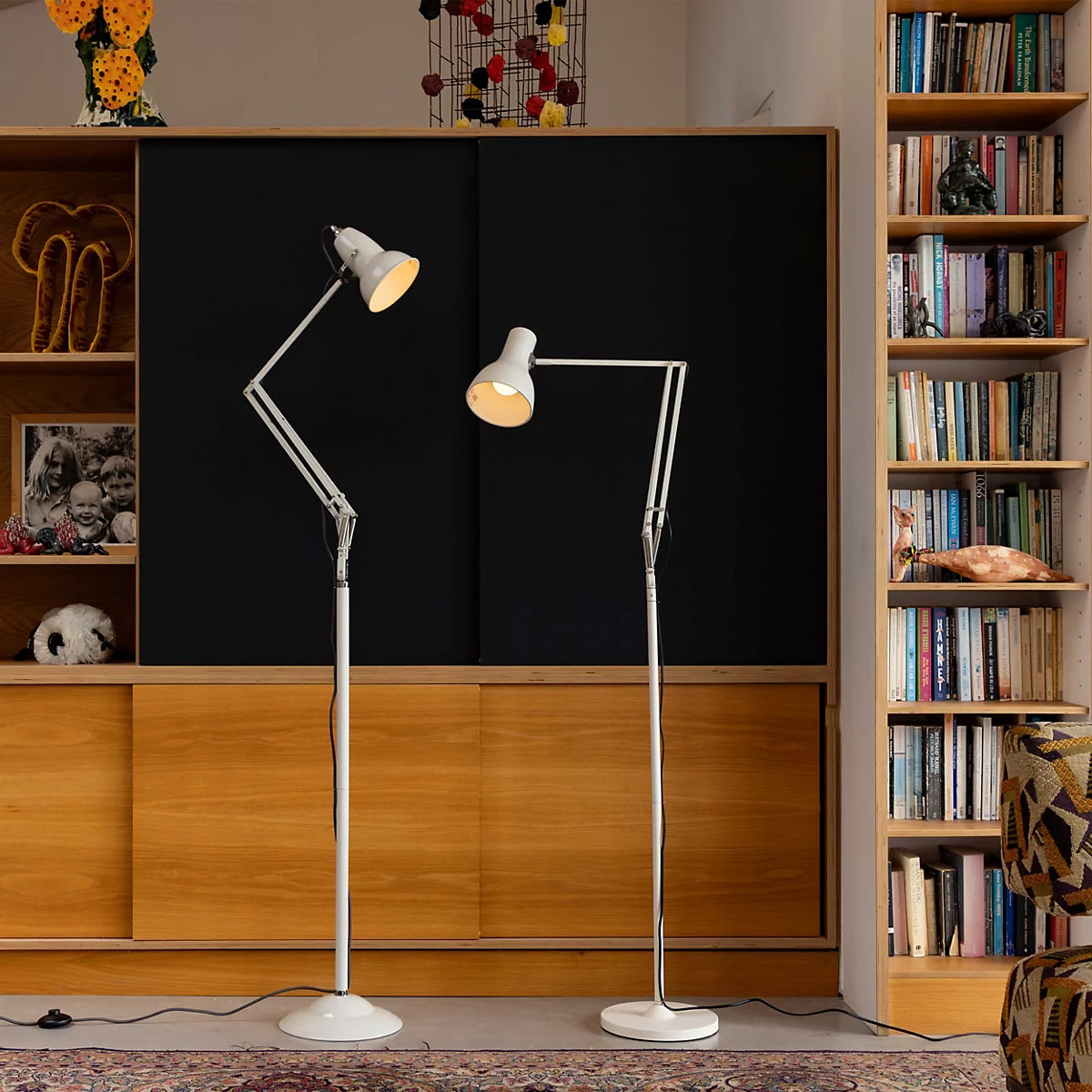 Two Anglepoise Type 75 floor lamps in white in front of wooden shelving