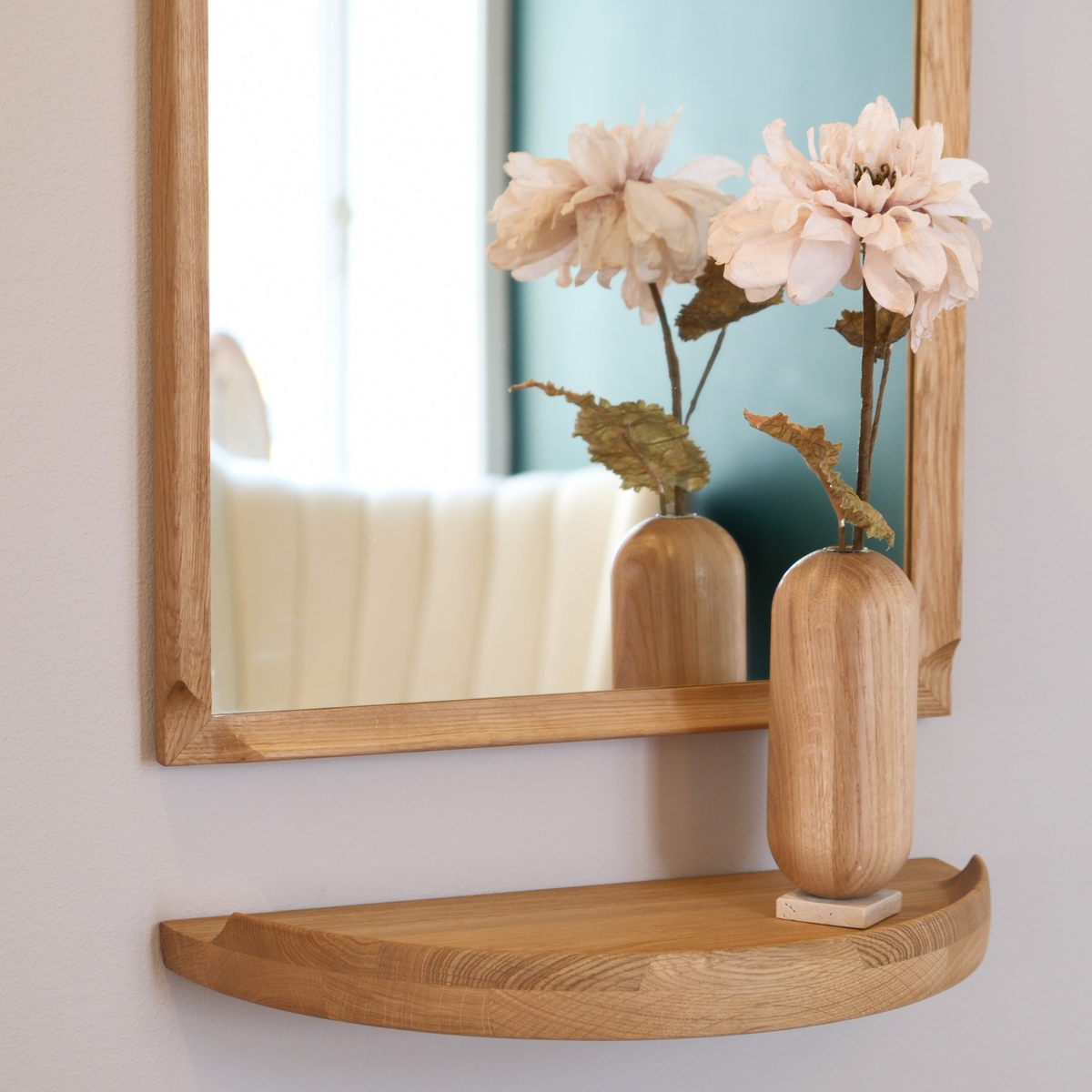 Aakjaer Arcus Mirror in natural oiled oak above a console shelf with a vase of pink flowers