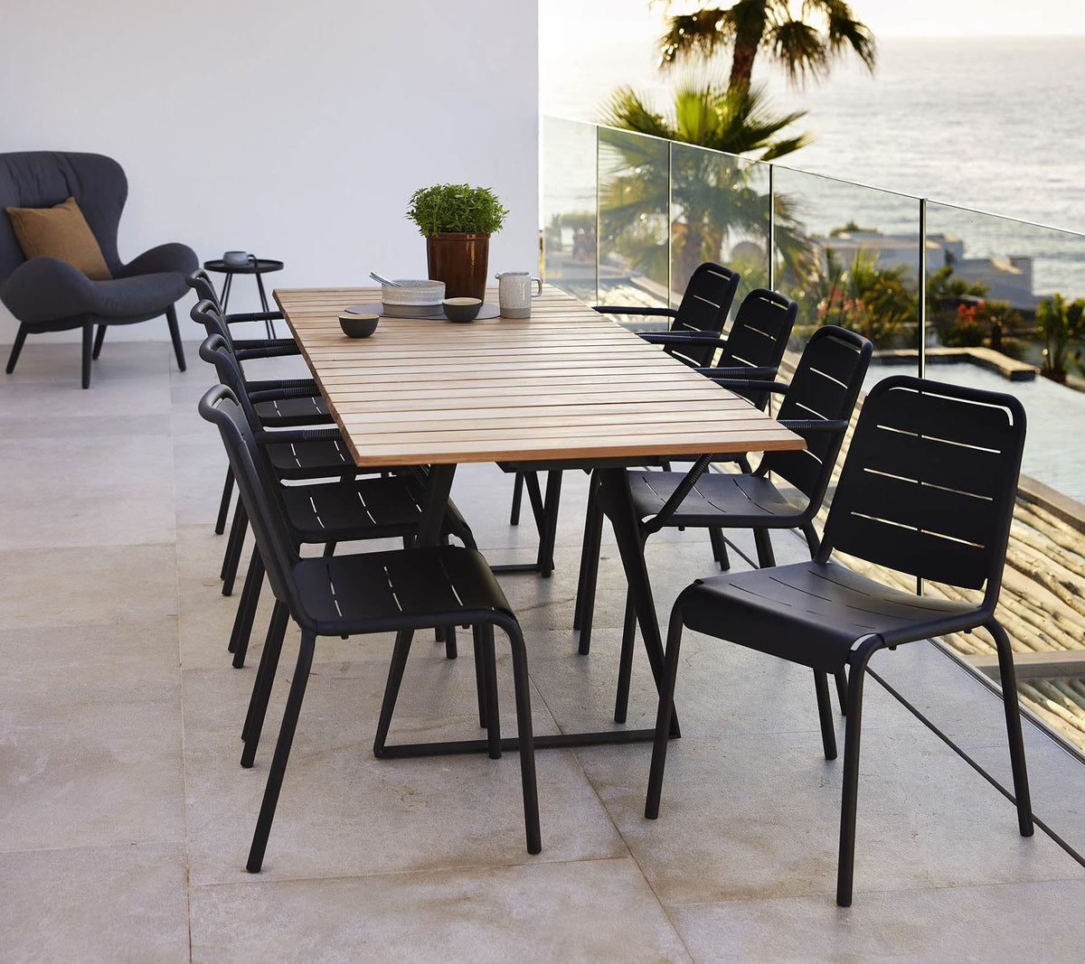 Cane-line Copenhagen Extendable Dining Table with black dining chairs, styled outdoors, teak and aluminum