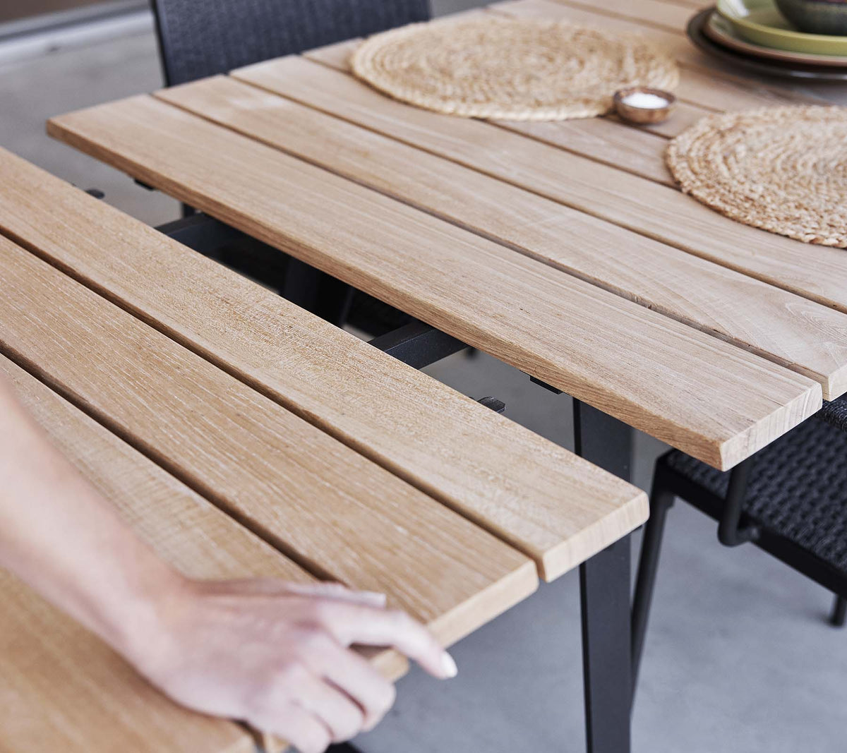 Detail of Cane-line Copenhagen Extendable Dining Table showing its slatted teak top, teak and aluminum