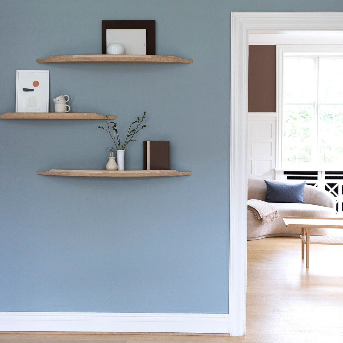 Aakjaer Arcus shelves in white oiled oak hung at staggered heights in a blue living room