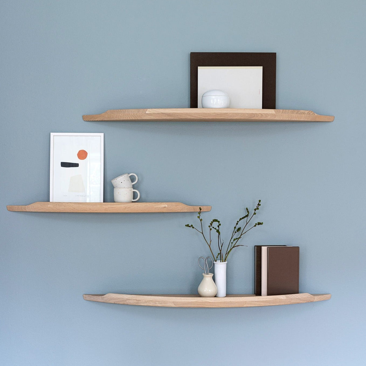 Three Aakjaer Arcus shelves in white oiled oak with prints and ceramics on a blue wall