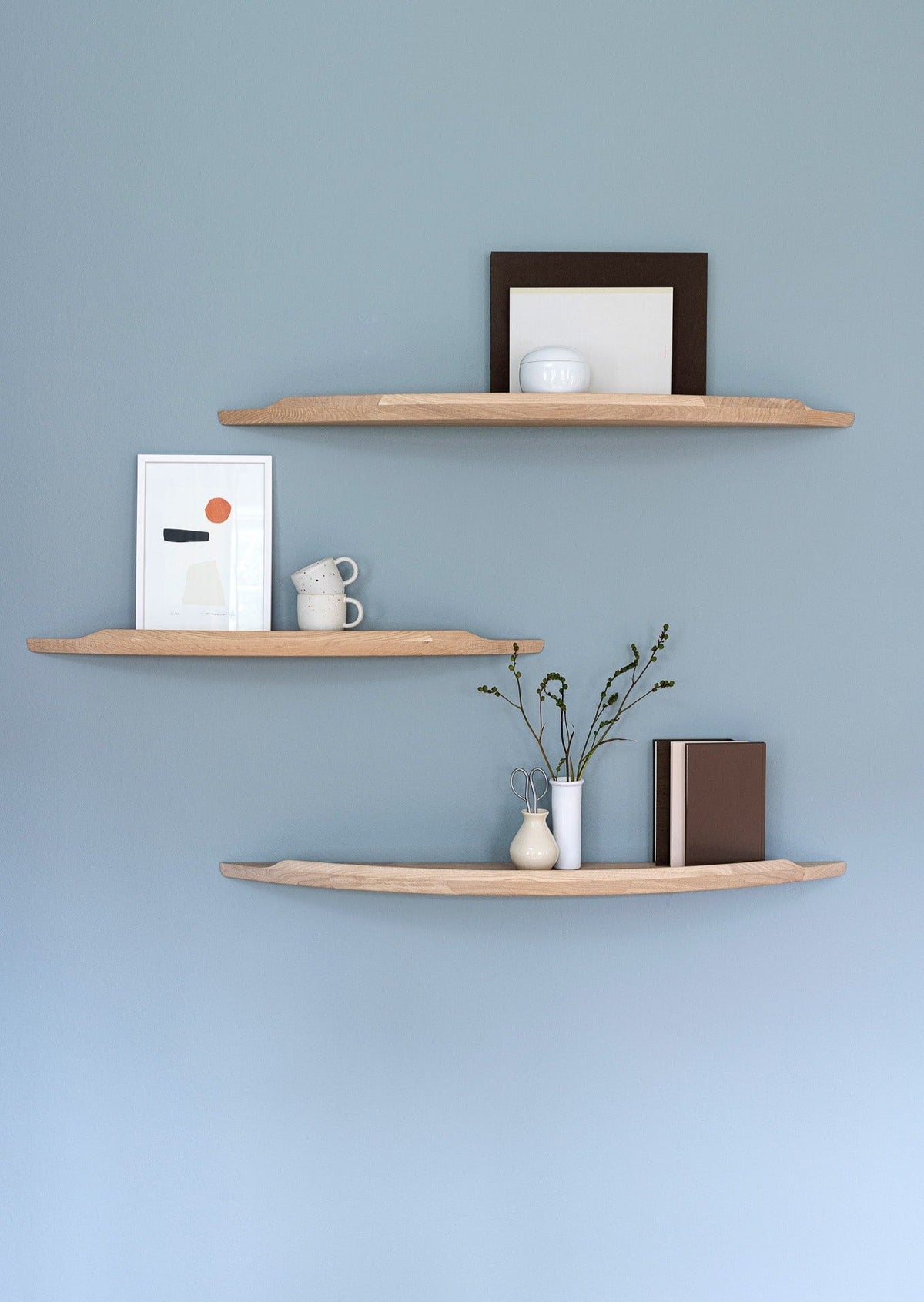 Three Aakjaer Arcus shelves in white oiled oak with prints and ceramics on a blue wall