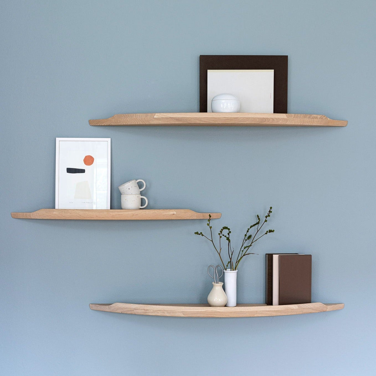 Three Aakjaer Arcus shelves in white oiled oak with prints and ceramics on a blue wall
