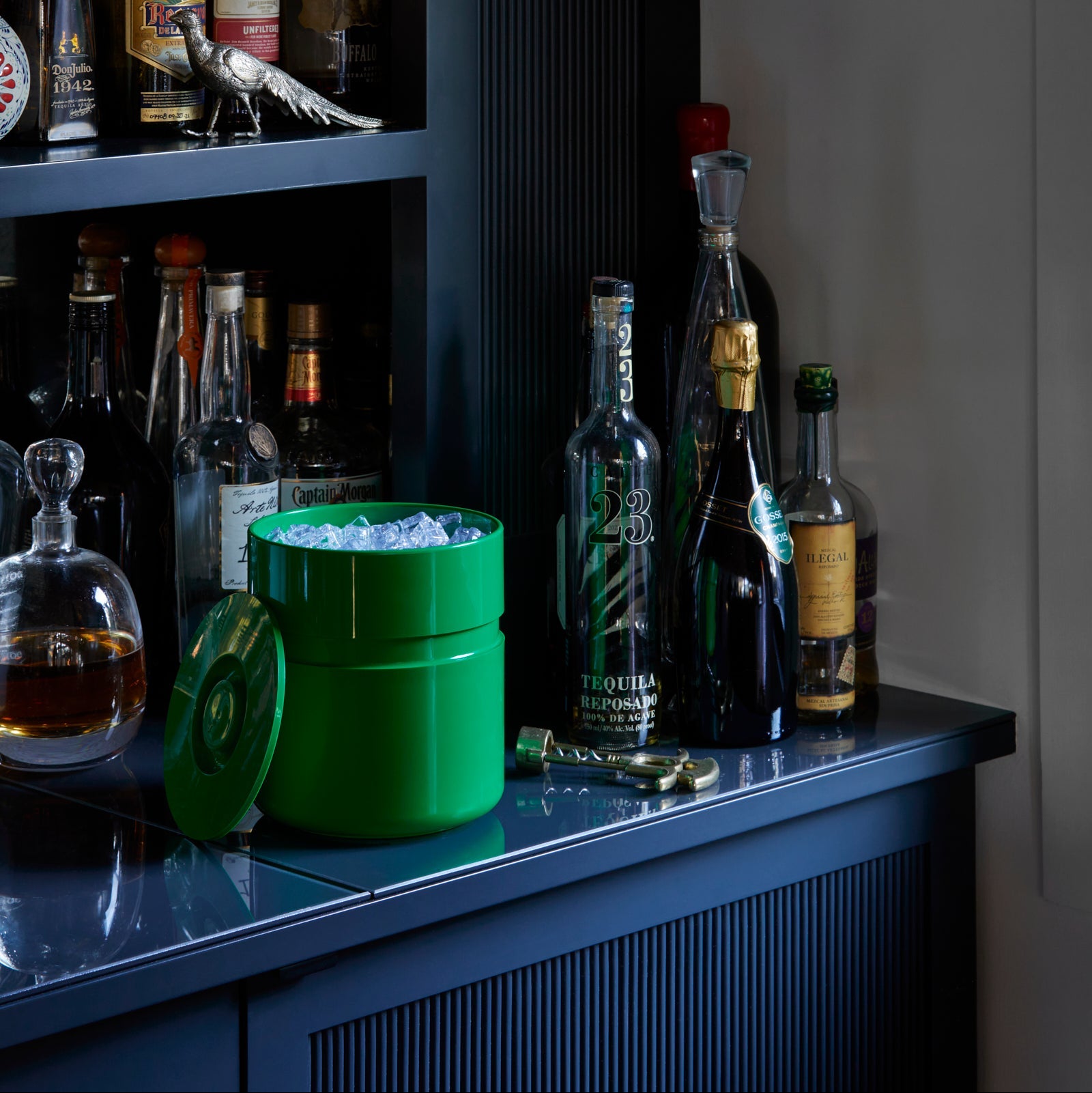Bar setup with various bottles and a green ice bucket on a dark surface.
