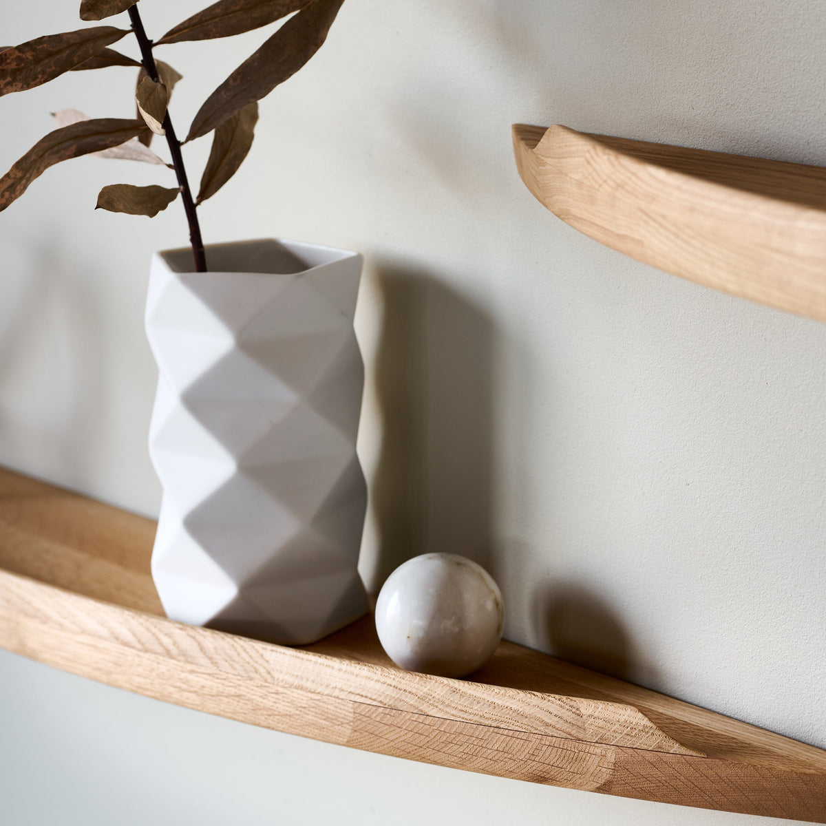 Aakjaer Arcus shelf in natural oiled oak styled with a white geometric vase and dried leaves