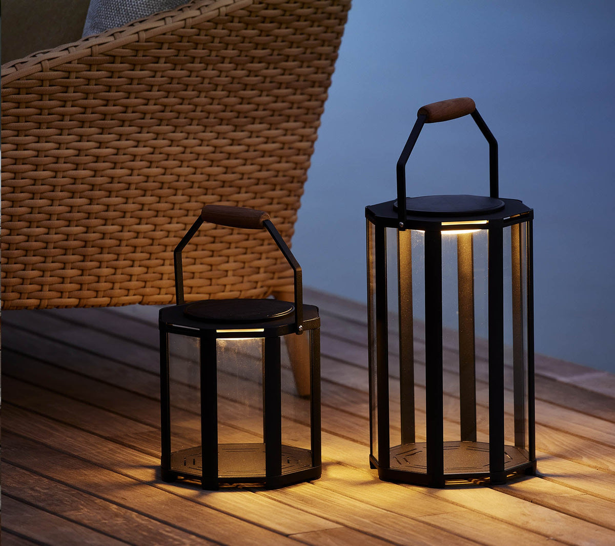 Two Cane-line Lightlux Lanterns lit beside a woven chair, powder-coated aluminum and glass, styled outdoors