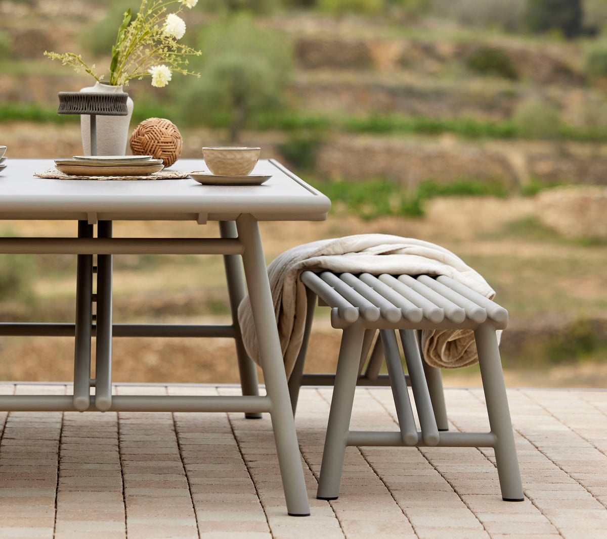 Cane-line Sticks Bench in Taupe at a Sticks dining table, styled outdoors, powder-coated aluminum