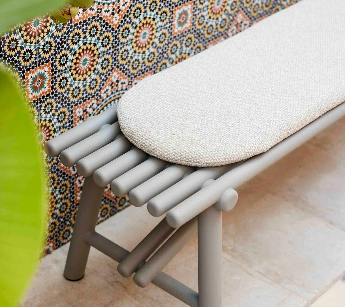 Cane-line Sticks Bench in Taupe styled against a patterned wall, powder-coated aluminum