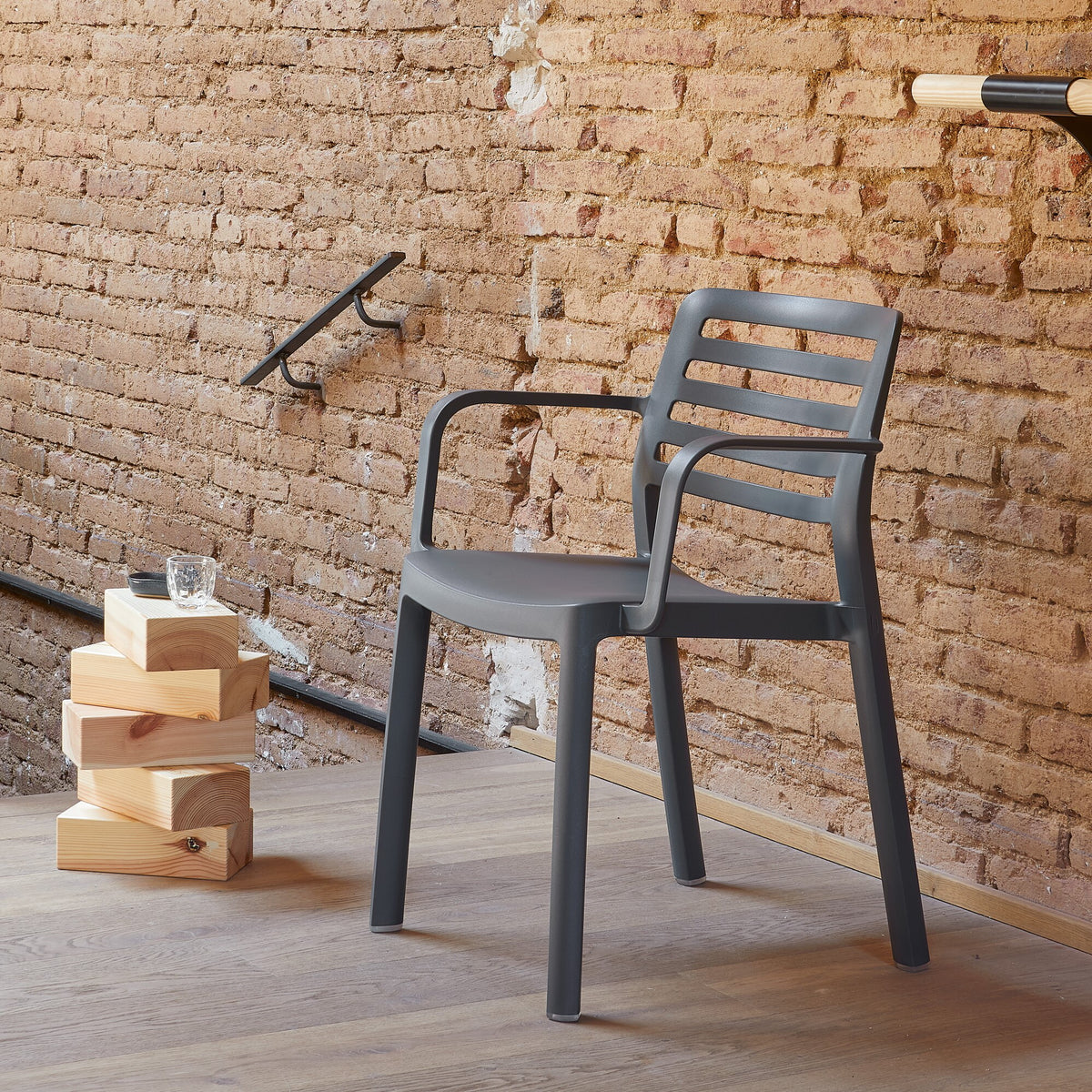 Garbar Wind Armchair in Dark Grey beside a brick wall on a wood floor