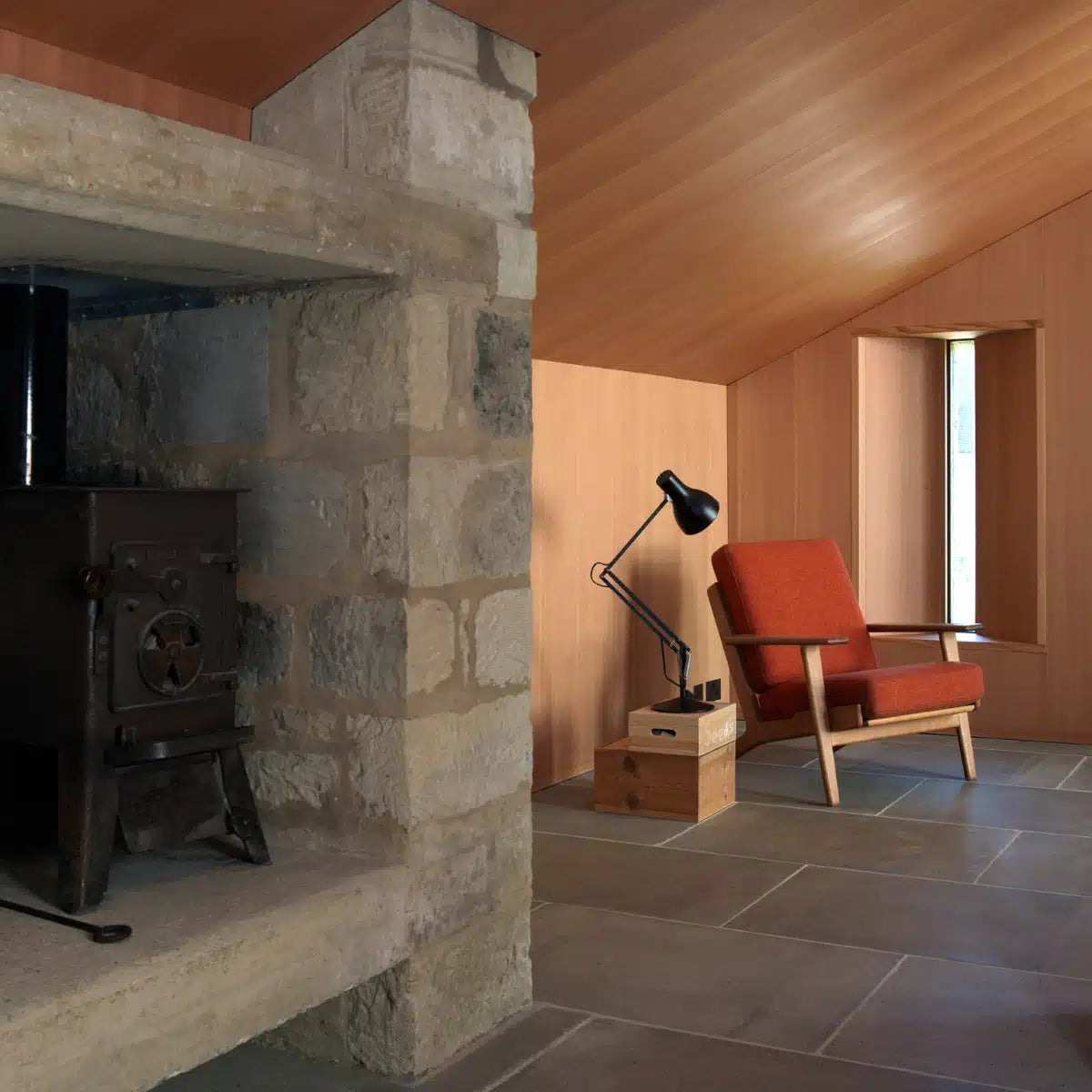 Anglepoise Type 75 desk lamp in black on a side table by a red armchair in a stone-walled living room