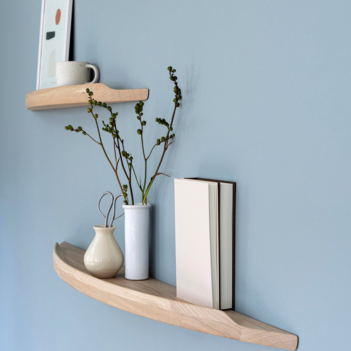 Aakjaer Arcus shelves in white oiled oak with vases and books on a blue living room wall