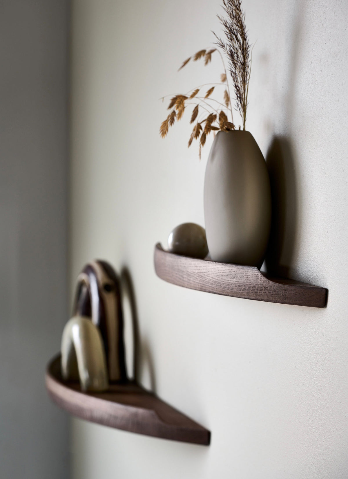 Side view of Aakjaer Arcus shelves in smoked oak holding ceramics and a tall vase