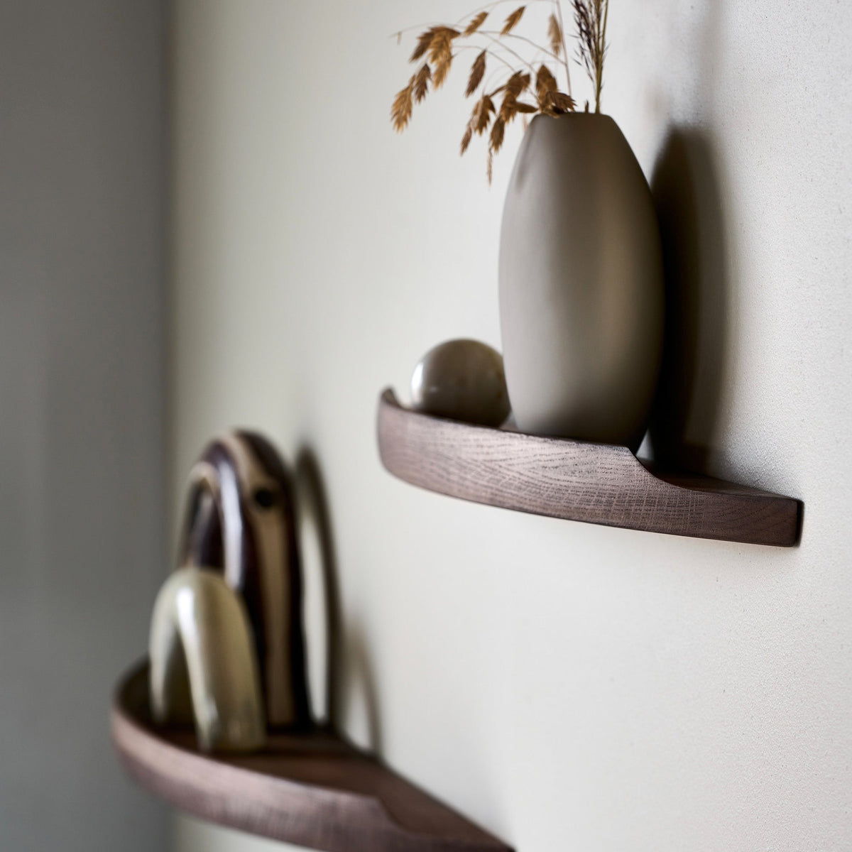 Side view of Aakjaer Arcus shelves in smoked oak holding ceramics and a tall vase
