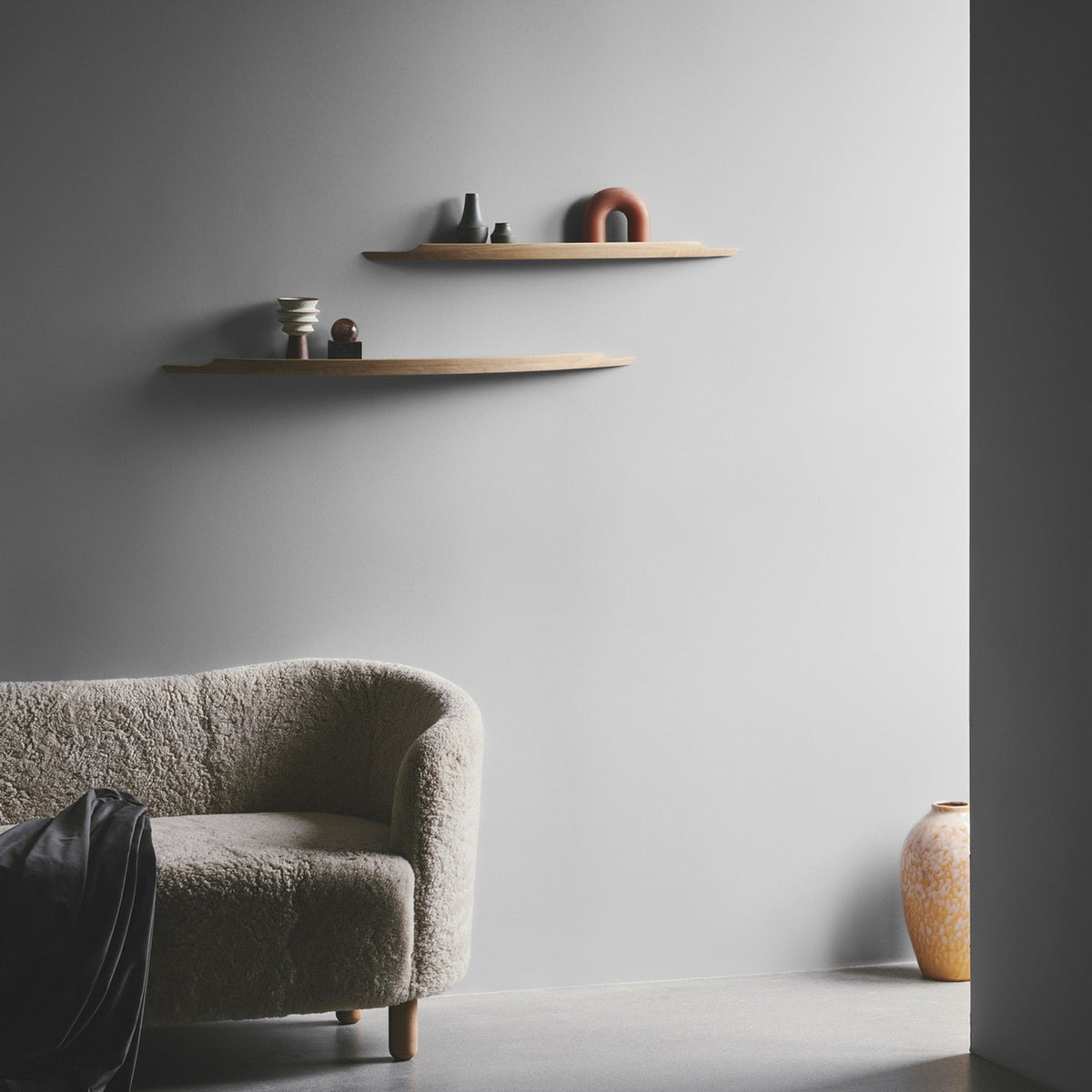 Aakjaer Arcus shelves on a gray wall beside a boucle armchair