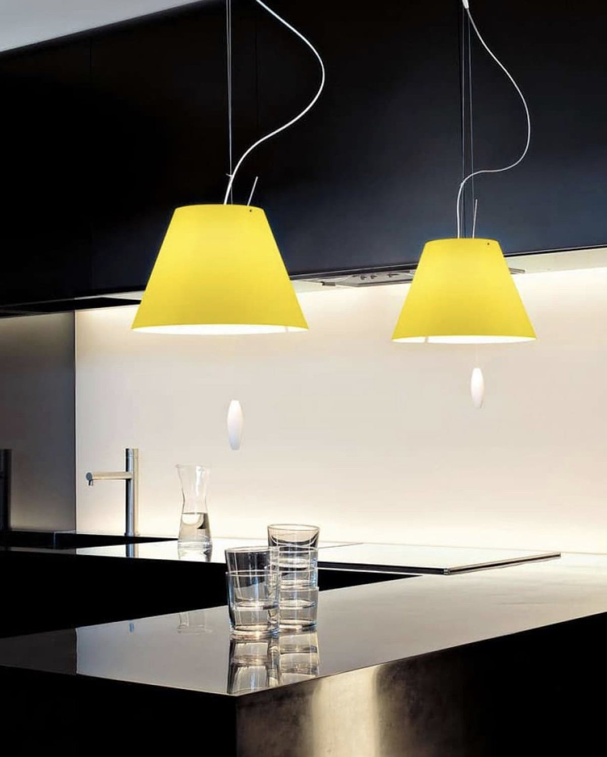 Luceplan Costanza Pendants with yellow shades over a dark kitchen counter