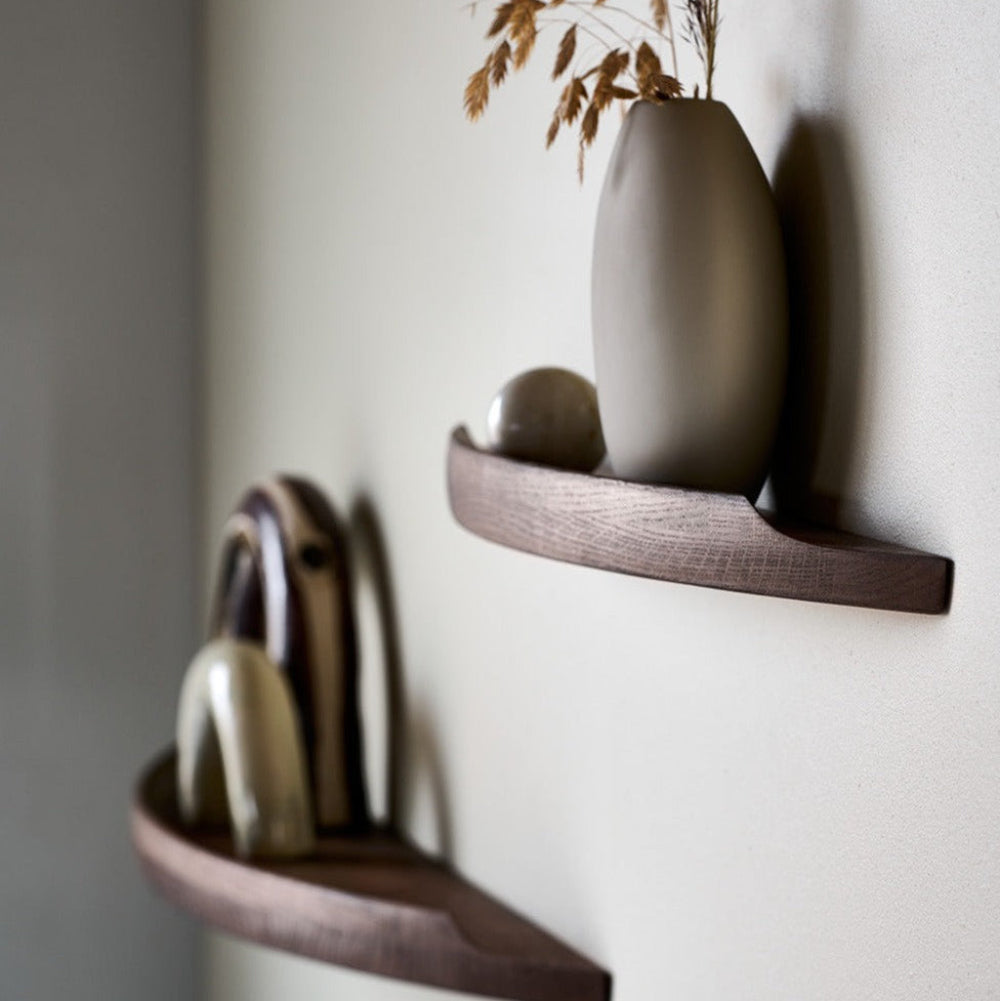 Side view of Aakjaer Arcus shelves in smoked oak holding ceramics and a tall vase