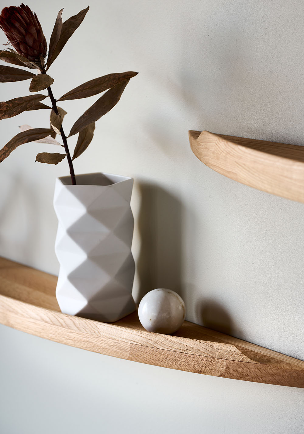 Close-up of an Aakjaer Arcus shelf in oak with a white geometric vase and dried leaves